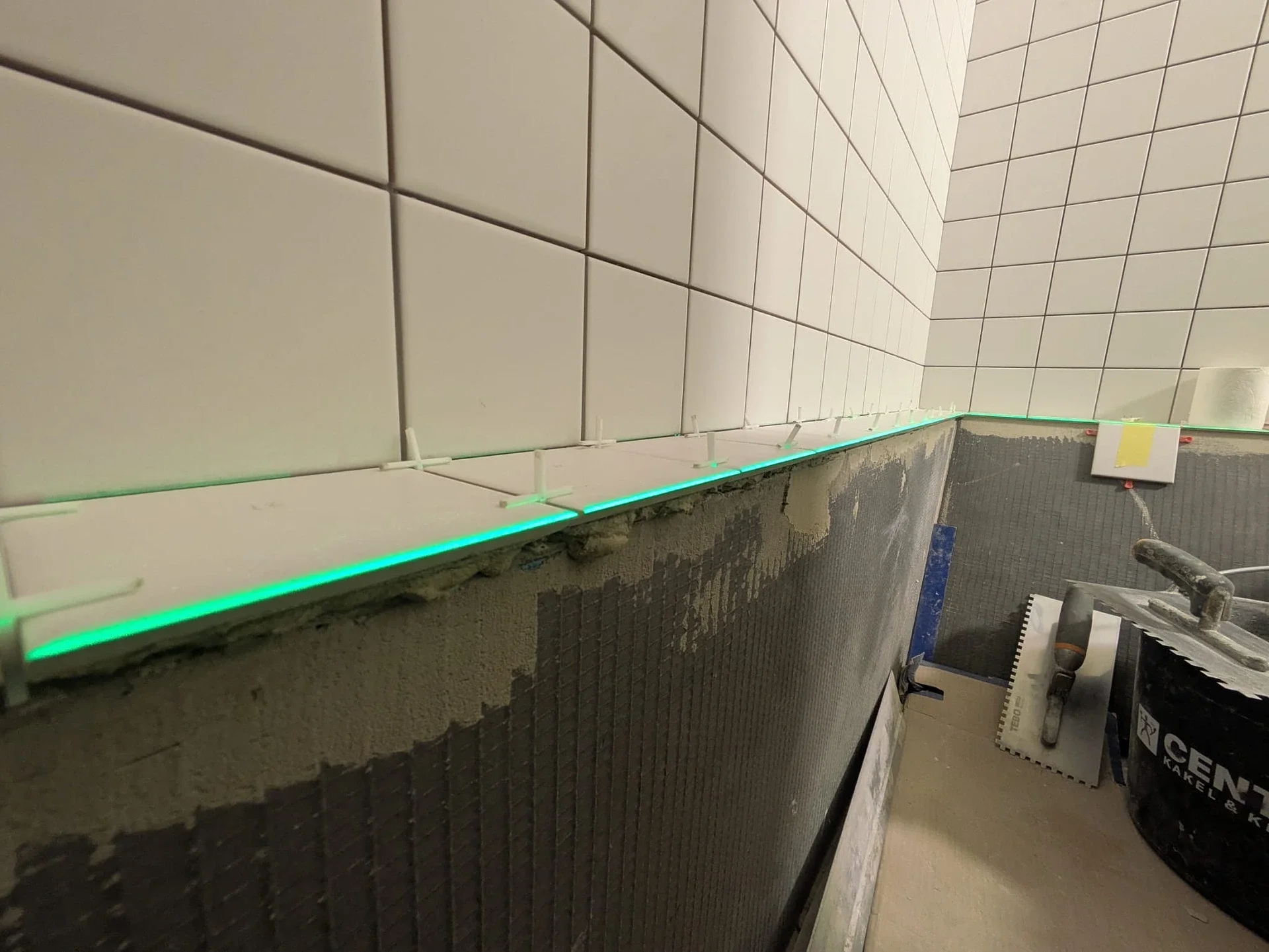 Kakelläggning pågår i badrum med grön LED-belysning längs kanten.