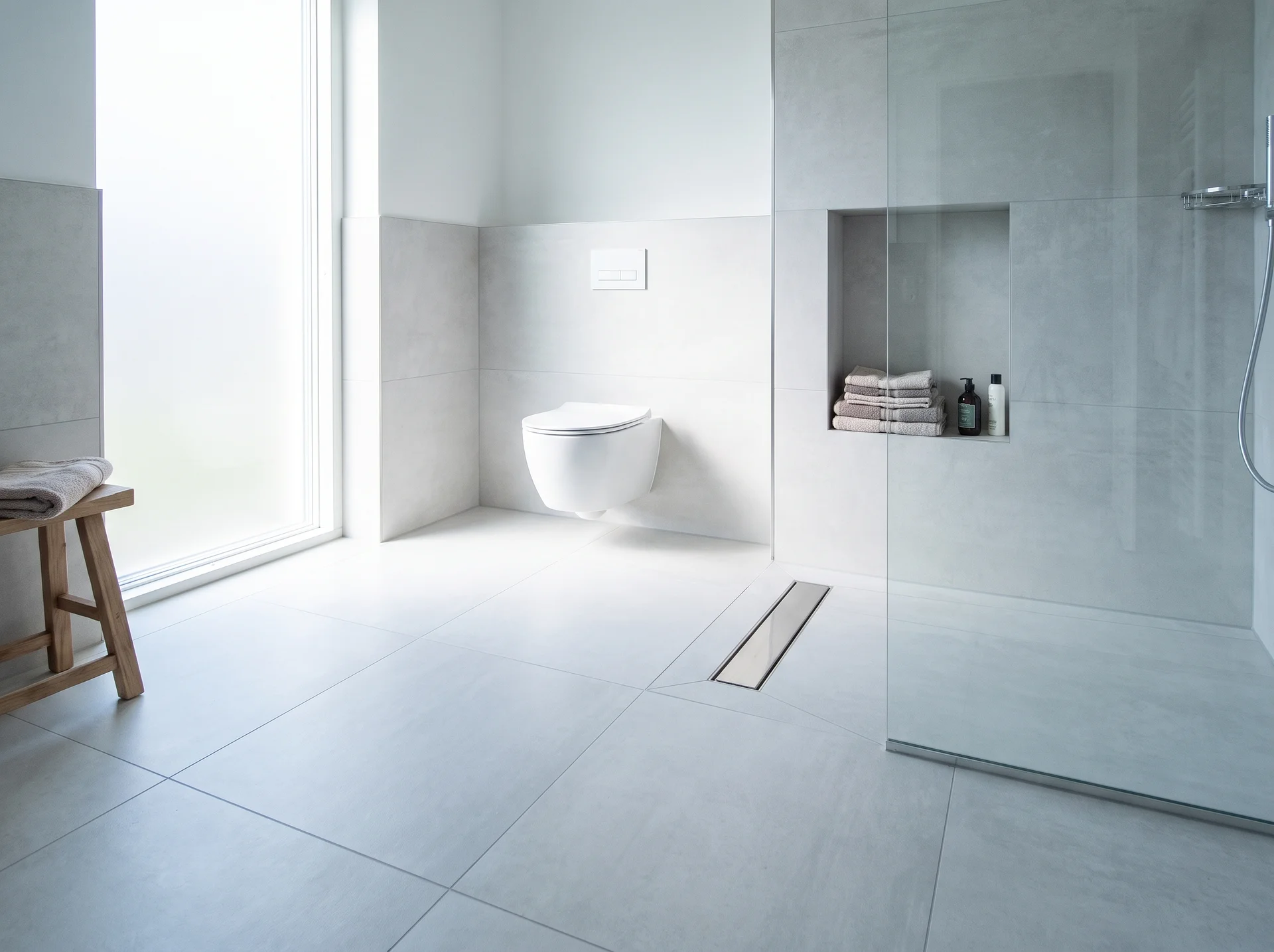 Modernt minimalistiskt badrum med walk-in dusch, vägghängd toalett och träpall.